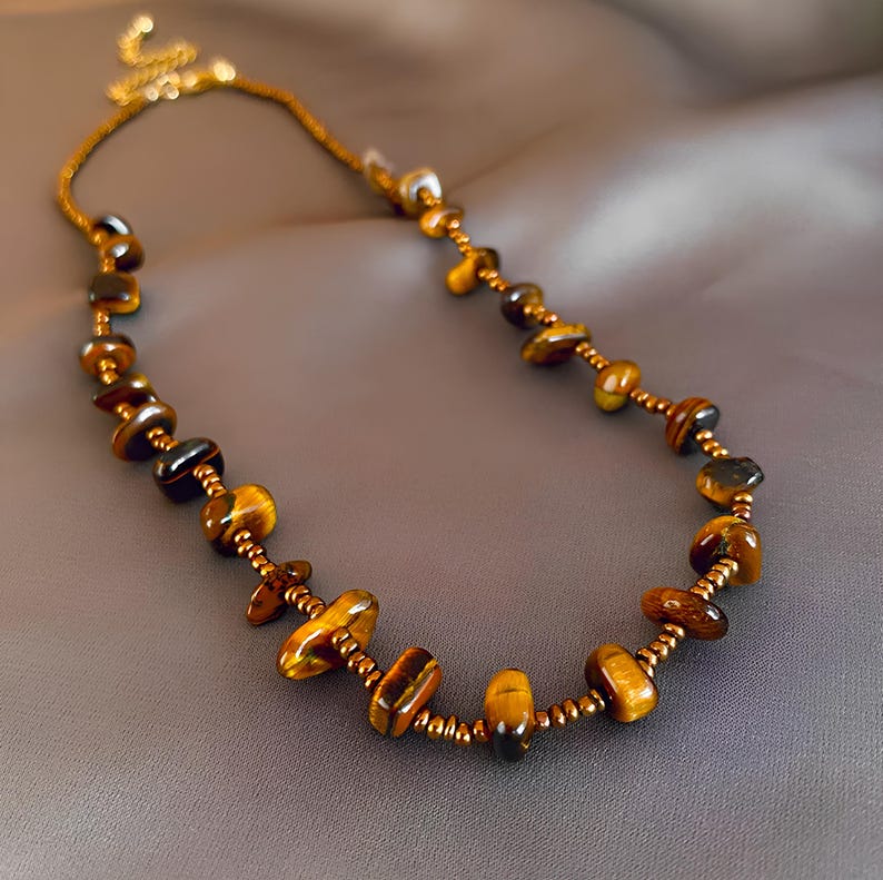 May include: A gold chain necklace with brown tiger's eye gemstone beads. The necklace is made with small gold beads between the larger tiger's eye beads.