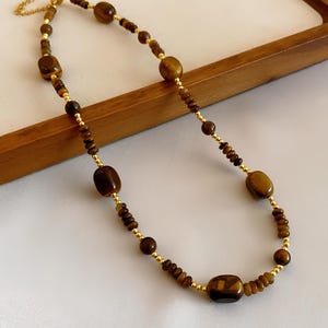 May include: A gold chain necklace with brown tiger's eye beads. The necklace features a mix of small and large beads.