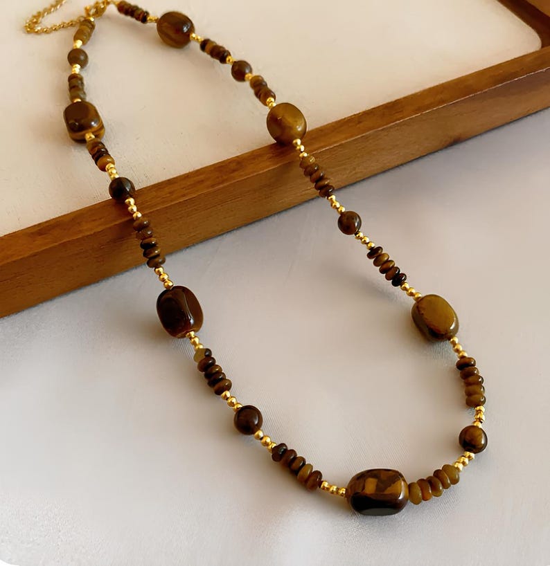 May include: A gold chain necklace with brown tiger's eye beads. The necklace features a mix of small and large beads.