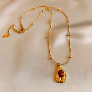 May include: A gold chain necklace with a teardrop-shaped pendant featuring a brown gemstone. The chain has small gold beads.