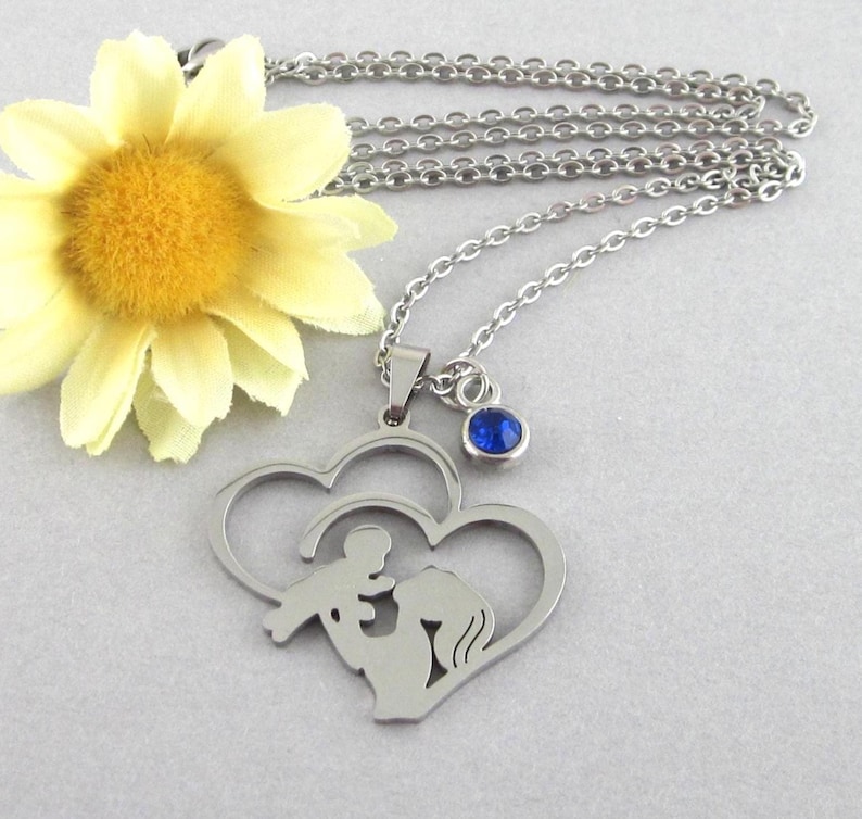 Stainless steel pendant that has a cut out silhouette of mother and baby in double heart. Choose a glass and stainless steel birthstone drop. Chain length choices, 17 inches through 20 inches. Pendant measures 1 3/8 long x 1 1/4 inches wide.