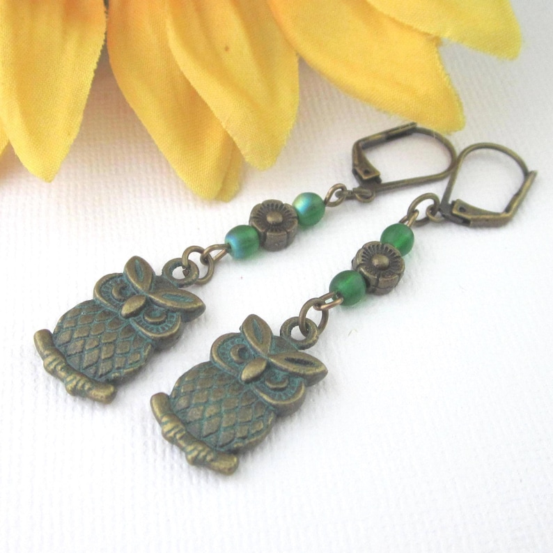 Bronze patina verdigris textured owl charm, lever back earrings with small textured daisy beads and smooth matte green seed beads. Dangle 2 1/2 inches, owl charms 19mm x 11mm