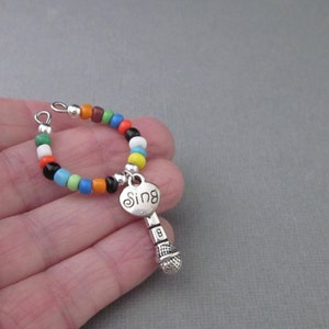 May include: A colorful beaded bracelet with a silver charm in the shape of a microphone with the word "Sing" on it.