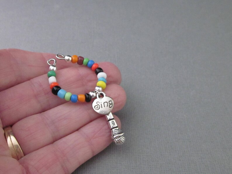 May include: A colorful beaded bracelet with a silver charm in the shape of a microphone with the word "Sing" on it.