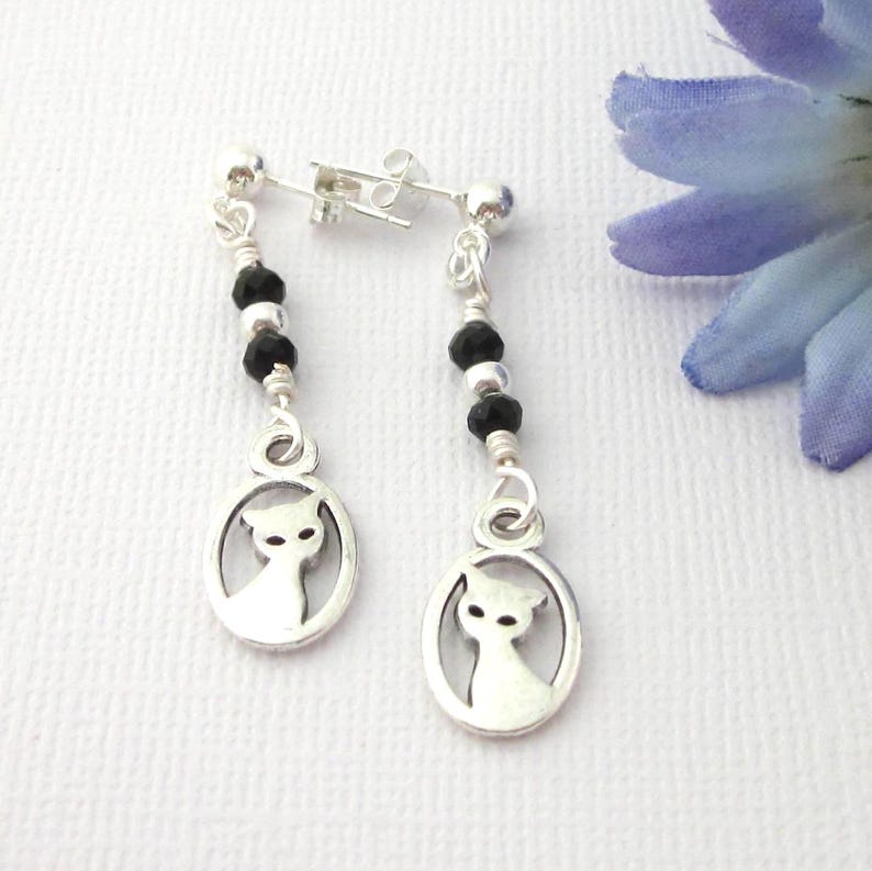 Short dangling cat in frame earrings with black and silver beads. Earrings posts and clutch are sterling silver. Length 1 5/8 inch. Cat in frame 9mm x 16 mm. Organza pouch included.