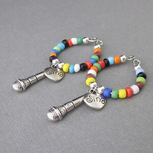 May include: Two colorful beaded hoop earrings with a silver microphone charm and a heart pendant that says "Sing".