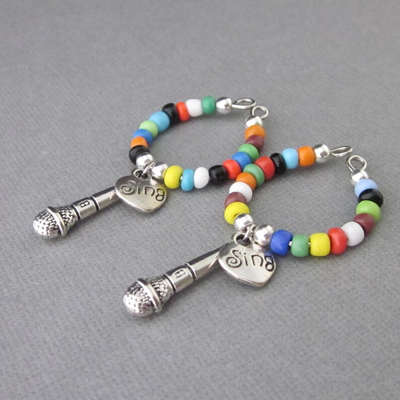 May include: Two colorful beaded hoop earrings with a silver microphone charm and a heart pendant that says "Sing".