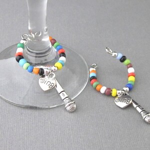 May include: Two colorful beaded wine glass charms with a microphone and heart charm that says "Sing".