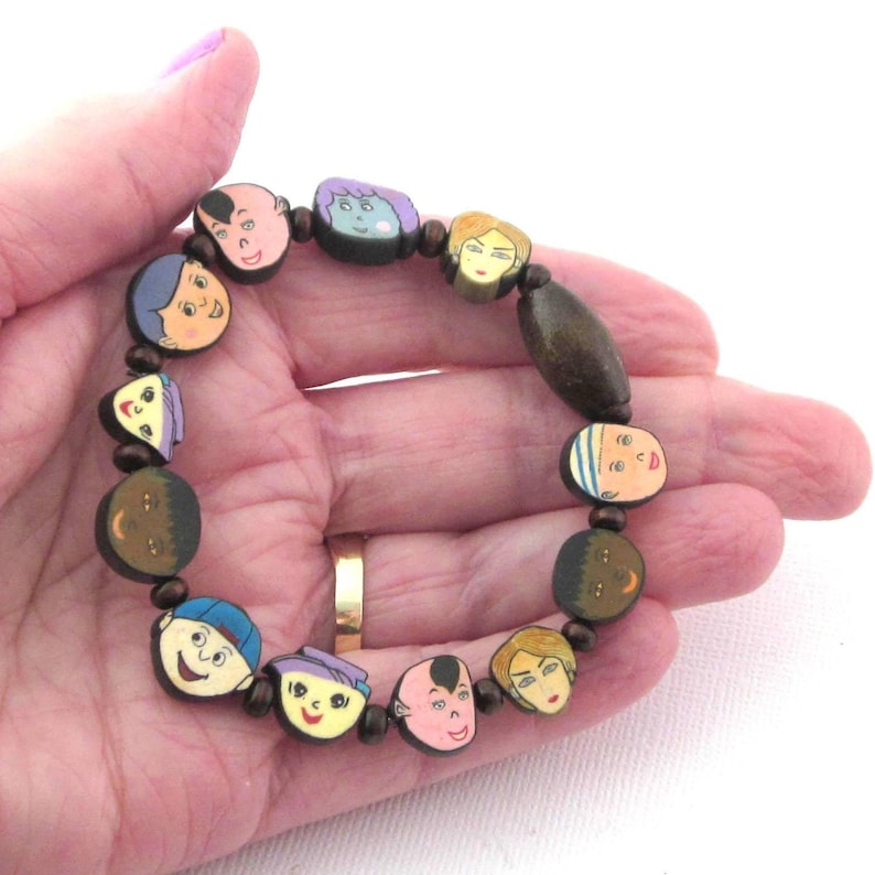 Stretch cord bracelet with flat wood beads with painted on faces, some children, some adults. Same on both sides. Faces separated with small round wood beads. Two sizes available 7 inch and 7 1/2 inch.