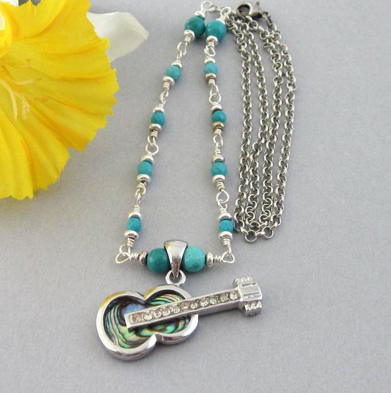 Guitar pendant necklace with partially beaded chain. The guitar has an inset of abalone shell and rhinestones. The linked beads are turquoise howlite and silver Heishi spacers.  Guitar measures 1 1/2 inch x 5/8 inch. Necklace 22  1/2 inches.