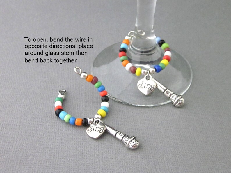 May include: Two colorful beaded wine glass charms with a silver microphone and heart charm with the word "Sing" on it.