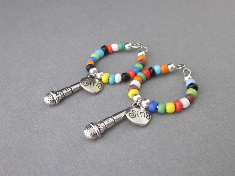 May include: Two colorful beaded hoop earrings with a silver microphone charm and a heart-shaped pendant that says "Sing".