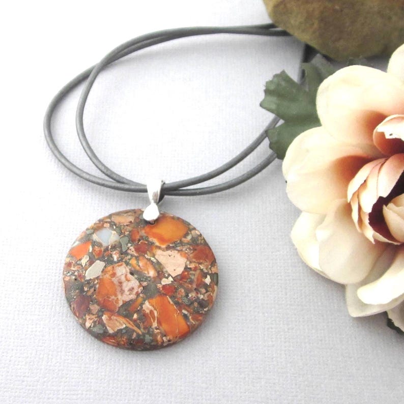 Synthetic jasper gemstone pendant in orange, gray and tan colors. Size 40 mm round. Backside in flat. Two gray leather 24 inch leather cords fasten with lobster clasp. Organza gift pouch included.