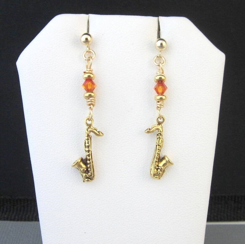 Very small gold plated dangling saxophone charm earrings with sparkling orange crystals. Post and clutches are 14k gold filled. Earrings dangle 1 3/4 inches, Sax charms 22mm x 12mm