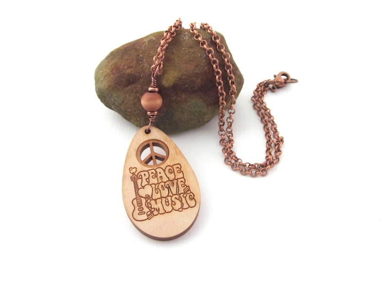Oval wooden pendant has engraved words peace, love, music and an acoustic guitar.  The pendant is accented with a round wood bead and two copper TierraCast Heishe spacers.  The copper plated rolo chain is 22 inches long. The pendant with the accent bead measures 2 5/8" long. Included is an organza gift pouch. The wood is lightweight making it comfortable to wear.
