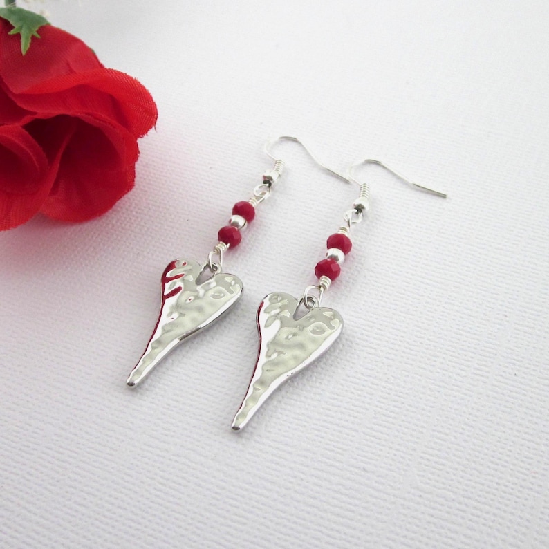 Hammered heart earrings with dark red crystals and sterling silver beads. Earrings measure 2.5 inches long measured from top of earring hooks. The hooks are hypoallergenic silver plated. Hearts measure 27 mm by 12 mm, faceted crystals 3 x 4 mm, and round silver 3 mm.