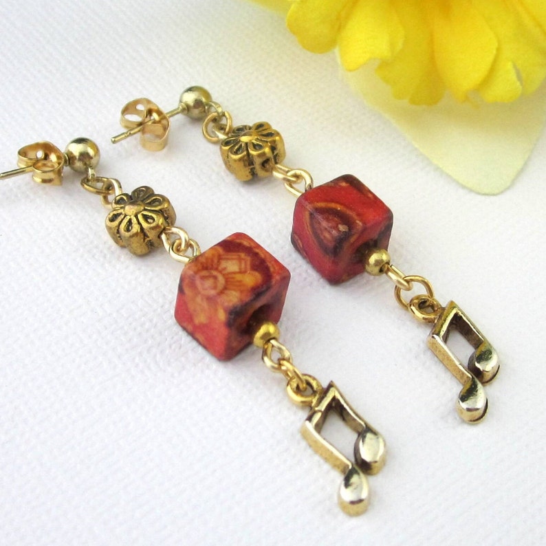 16th note charm earrings with reddish orange pansy flower wooden cube beads and gold textured flower beads. Earrings dangle: 2 1/8”. Antiqued gold 16th note charms 15 mm x 10 mm. Wooden  Pansy Cube beads 8 mm.