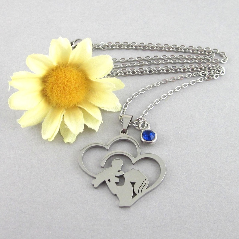 Stainless steel pendant that has a cut out silhouette of mother and baby in double heart. Choose a glass and stainless steel birthstone drop. Chain length choices, 17 inches through 20 inches. Pendant measures 1 3/8 long x 1 1/4 inches wide.