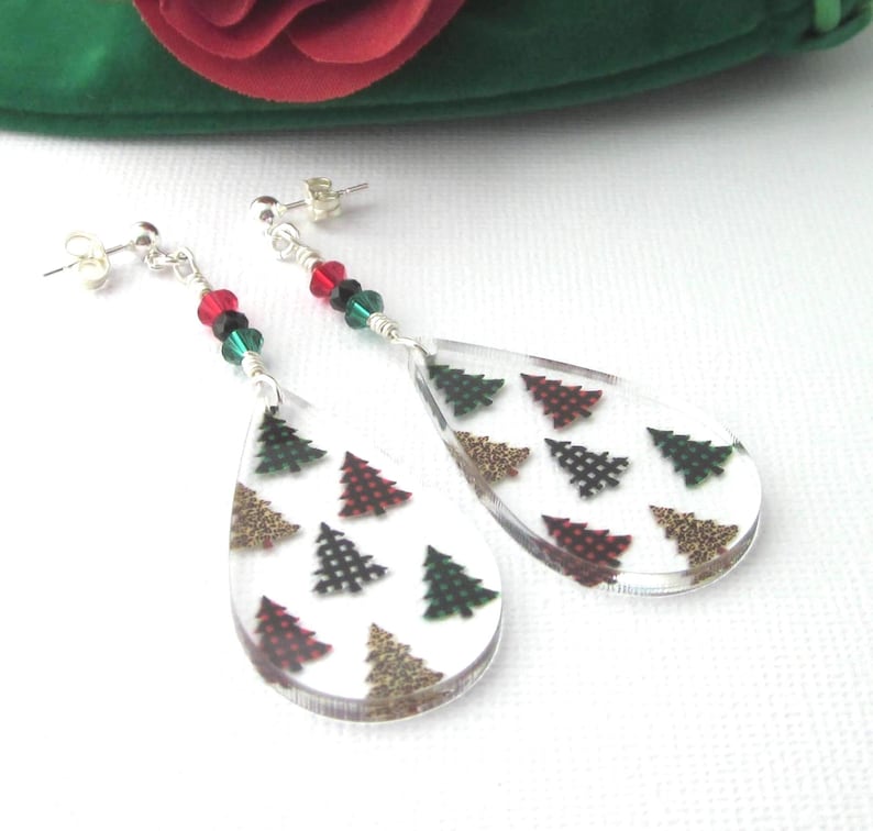 Acrylic teardrop shape drops have Christmas trees with buffalo plaids and leopard prints. Sparkling red, green and black crystals and sterling silver posts and clutches. Green velour gift pouch included. Earrings dangle 2 5/8 inches long. The acrylic teardrop alone 1 ½ inches long x 7/8 inch wide x 1/8 inch thick. Prestige crystal bicones 4 mm. Glass rondells 3 mm x 2 mm.