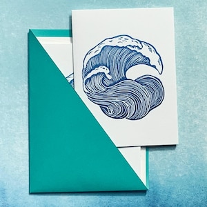 May include: White greeting cards with a blue wave design are nestled inside a teal envelope. The wave illustration features detailed lines, creating a sense of movement. The envelope's triangular flap adds a modern touch.