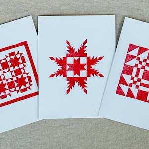 Op de afbeelding: Drie witte kaarten met rode geometrische patronen erop gedrukt. De patronen zijn een stervormige uitbarsting, een vierkant met een ster in elke hoek en een vierkant met een rasterpatroon.