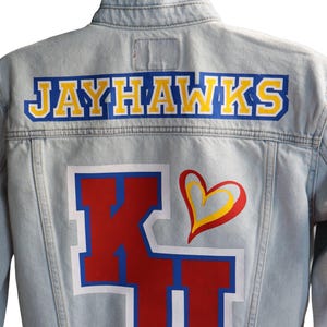 May include: Light blue denim jacket with "JAYHAWKS" in yellow letters outlined in blue across the shoulders. Below, a large red "KU" with a white border and a yellow and red heart design.
