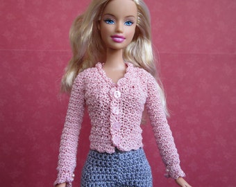 May include: A pink crocheted cardigan with a button closure and a matching gray crocheted skirt. The cardigan has long sleeves and a scalloped hem.