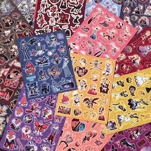 Peut inclure: Une collection de plusieurs planches d'autocollants représentant divers personnages animés de Hazbin Hotel et Helluva Boss. Les planches présentent des designs variés dans des palettes de couleurs rouge, bleu, jaune et violet avec diverses poses.