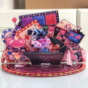 Könnte beinhalten: Ein mehrschichtiger Acryl-Aufsteller mit Charakteren aus Hazbin Hotel in einer Casino-Umgebung. Das Design umfasst einen Spielautomaten, Spielkarten, ein Rouletterad und eine Figur mit einem Fernseher als Kopf. Die Basis ist ein Halbkreis.