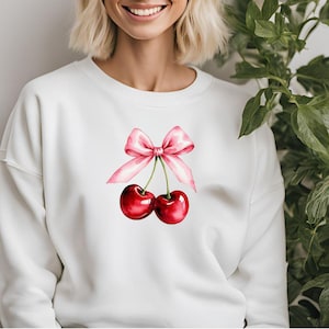May include: White sweatshirt with a pink bow and two red cherries on the front.