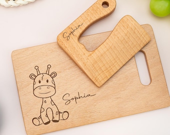 May include: A wooden cutting board and a matching chopper. The cutting board features a giraffe illustration and the name "Sophia". The chopper has a handle with the name "Sophia" engraved. Both items are made of light-colored wood.