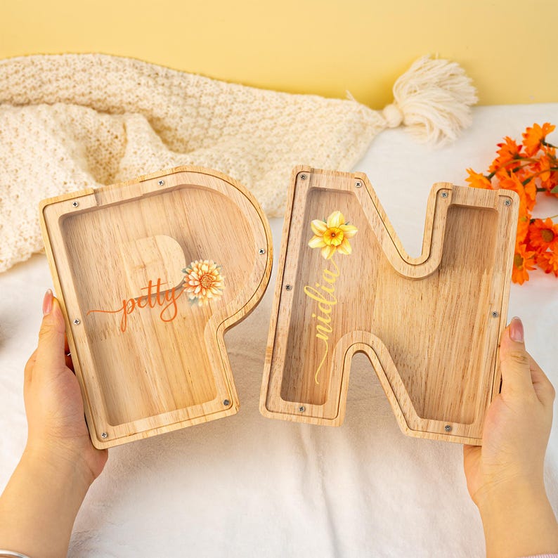 May include: Two wooden money boxes shaped like the letters "P" and "N". The "P" has the word "petty" written on it in cursive and the "N" has the word "midlife" written on it in cursive. Both money boxes have a slot on the top for coins and a clear plastic window on the front.