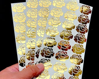 May include: Five vertical sheets of adhesive stickers featuring a repeating pattern of metallic gold rose designs. Each sticker is a stylized, shiny gold rose silhouette arranged in neat rows on a plain white backing paper for easy application.