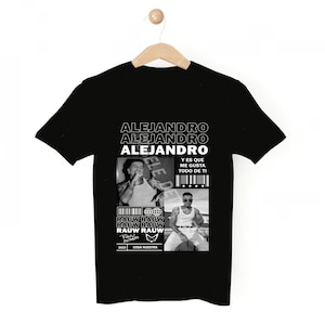 May include: Black t-shirt with a white graphic print featuring a portrait of a man with the text "ALEJANDRO" repeated three times and "RAUW RAUW" repeated four times. The text "Y ES QUE ME GUSTA TODO DE TI" and "COSA NUESTRA" are also included in the graphic.