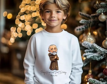 May include: A white sweatshirt featuring a cartoon illustration of Padre Pio in a brown robe. The text "Pray Hope and Don't Worry" and "Padre Pio" are printed below the image. The sweatshirt is worn by a young person.