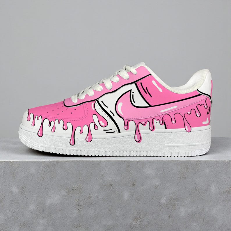 以下が含まれることがあります： ピンクと白のアスレチックシューズ、ユニークなドリップデザイン。 ピンクのアッパーに白いスウッシュと靴紐が付いています。 黒いアウトラインがドリップ効果とデザイン要素を定義しています。 ソールは白です。