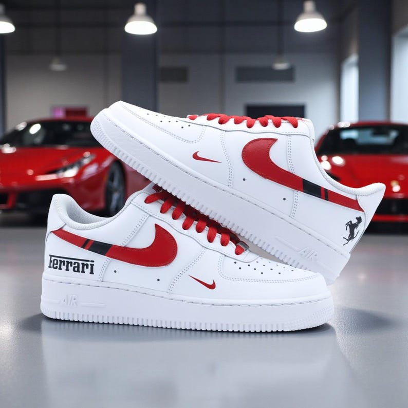 May include: White sneakers with red accents, including the Nike swoosh and laces. The word "Ferrari" is printed on the side. A black and red stripe detail is visible. The shoes are displayed in front of a red sports car.