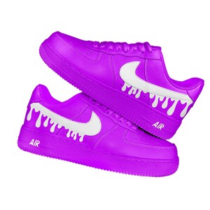 May include: A pair of vibrant purple trainers with white detailing. The shoes display a white Nike swoosh and white dripping paint effects. The word "AIR" is printed in white on the side of each shoe. The trainers are set against a white background.