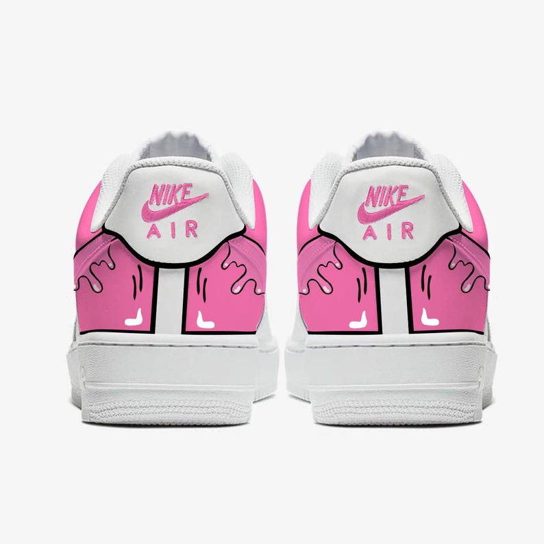 以下が含まれることがあります： ピンクのアクセントが付いた白いナイキエアフォース1スニーカーのペア。かかとには、ピンクのナイキエアロゴが付いた白いパネルがあります。ピンクのペイントのようなデザインが靴の背面を滴り落ちています。靴は白い背景にあります。