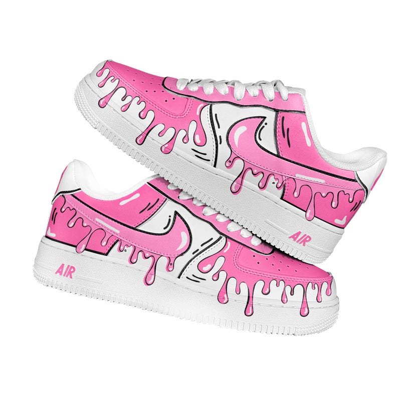 以下が含まれることがあります： ピンクと白のスニーカーのペアで、ユニークなドリップデザインが施されています。靴は白いソールと靴紐が特徴で、側面に「AIR」の文字がプリントされています。ピンクの塗料が靴の側面を伝って滴り落ちているように見えます。