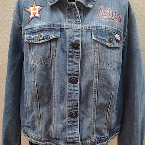 Peut inclure: Une veste en jean bleue avec un patch en forme d'étoile avec un "H" blanc sur la poitrine gauche et un patch "Astros" sur la poitrine droite.