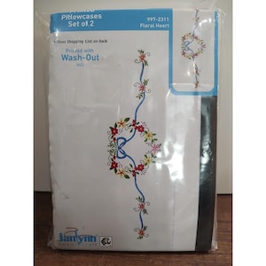 May include: A set of two white pillowcases with a floral heart design. The design features a blue ribbon, red and yellow flowers, and green leaves. The packaging includes the text "Printed Pillowcases Set of 2" and "Floral Heart".