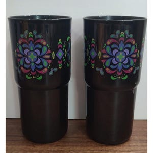 May include: Two black tumblers with a colorful floral design. The design includes purple, blue, green, pink, and yellow accents. The tumblers are made of a glossy material and have a two-part design.