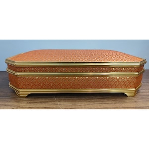 May include: An orange and gold decorative box with a patterned fabric top and sides. The box has gold trim and a rectangular shape. The box is sitting on a wooden surface.