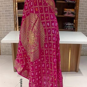 May include: A bright pink dupatta with detailed gold patterns. The fabric is draped over a mannequin, displaying a large central design and ornate borders. The text "Dupatta wala's" and "D no A800" are visible.