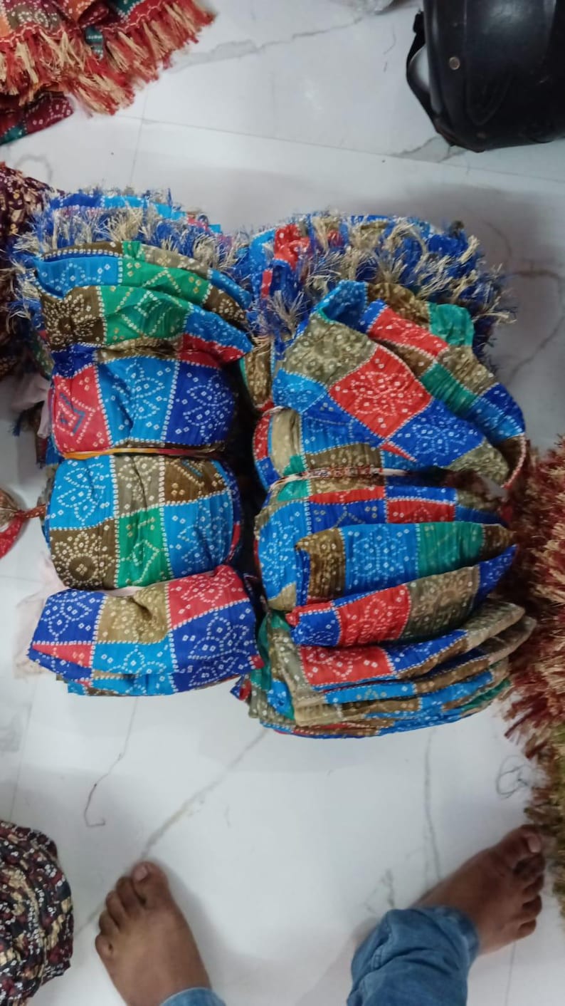 K&ouml;nnte beinhalten: Stapel bunter Stoff-Kopfbedeckungen mit geometrischen Mustern in Rot, Blau, Gr&uuml;n und Braun. Die Kopfbedeckungen sind gefaltet und geb&uuml;ndelt, einige mit dekorativen Fransen.