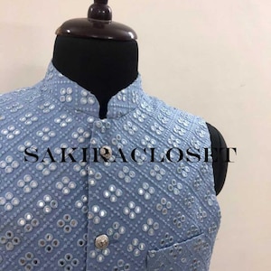 May include: A light blue vest with a geometric pattern of small mirrors and a mandarin collar. The vest has a single pocket and a silver button closure. The text "SAKIRACLOSET" is printed across the front of the vest.