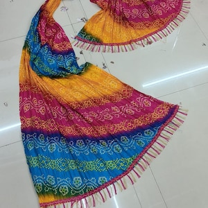 K&ouml;nnte beinhalten: Ein lebendiger, mehrfarbiger Schal mit Bandhani-Muster. Der Schal weist einen Farbverlauf aus Gelb, Rosa, Blau und Gr&uuml;n auf. Die Kanten sind mit Fransen versehen. Der Stoff scheint leicht und flie&szlig;end zu sein.