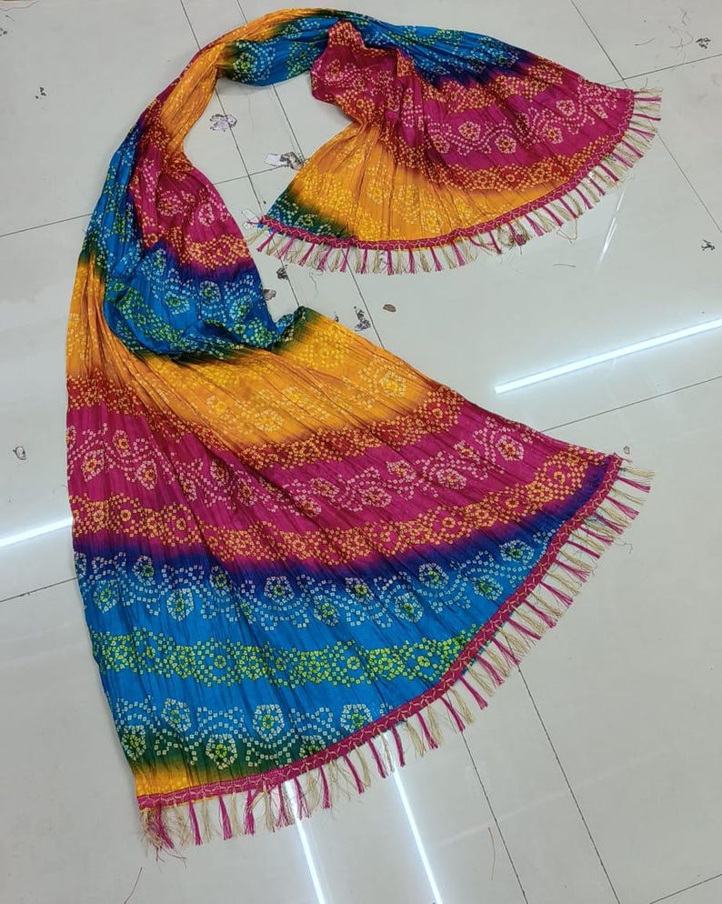 K&ouml;nnte beinhalten: Ein lebendiger, mehrfarbiger Schal mit Bandhani-Muster. Der Schal weist einen Farbverlauf aus Gelb, Rosa, Blau und Gr&uuml;n auf. Die Kanten sind mit Fransen versehen. Der Stoff scheint leicht und flie&szlig;end zu sein.