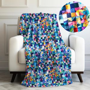 May include: A colorful throw blanket with a geometric pattern of squares and triangles in shades of blue, green, yellow, pink, and red. The blanket is draped over a white armchair.